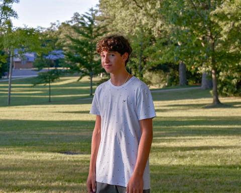 a young man standing in a park holding a frisbee