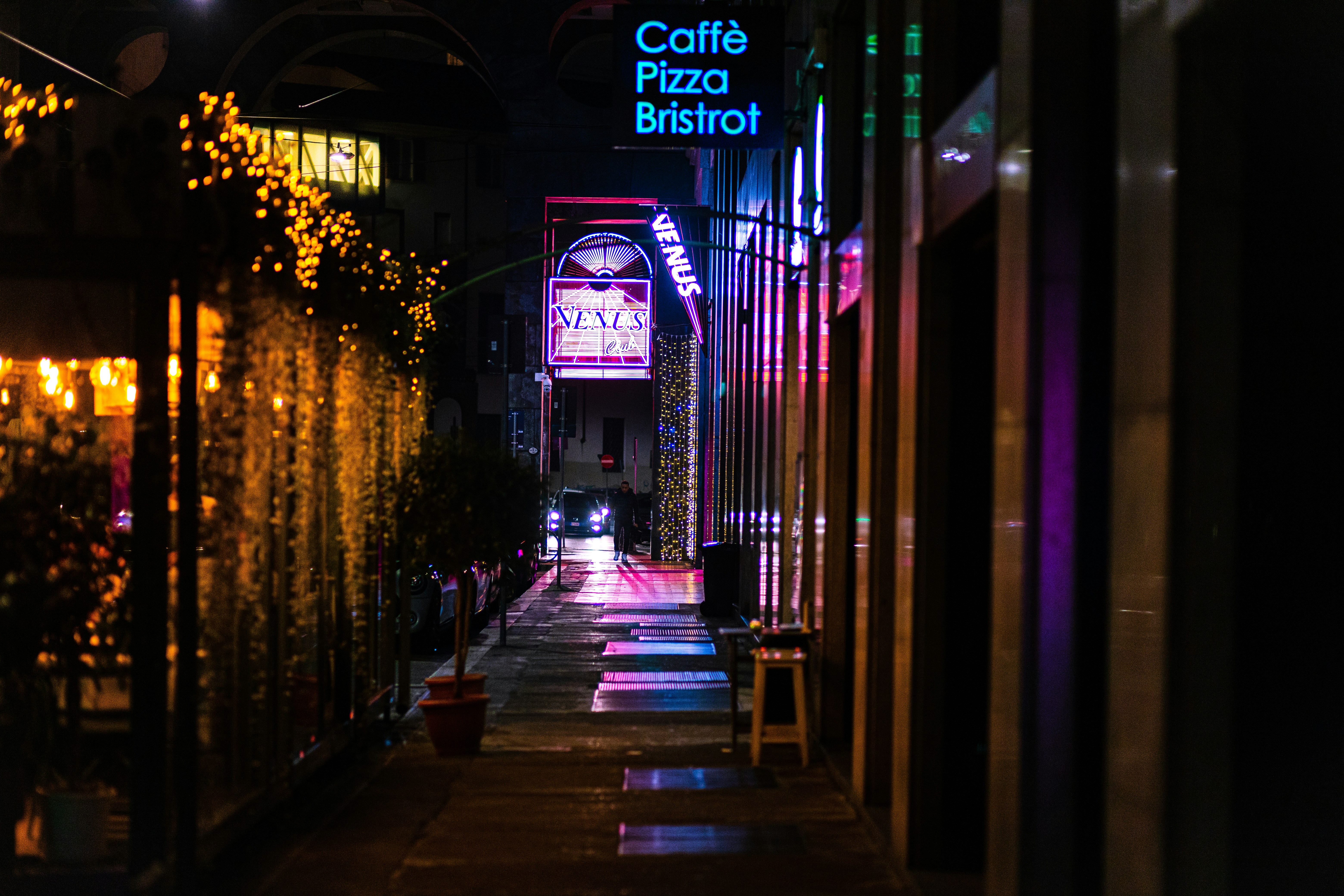 a street at night with a cafe sign lit up