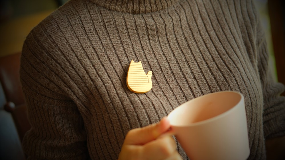 a person holding a cup with a cat pin on it