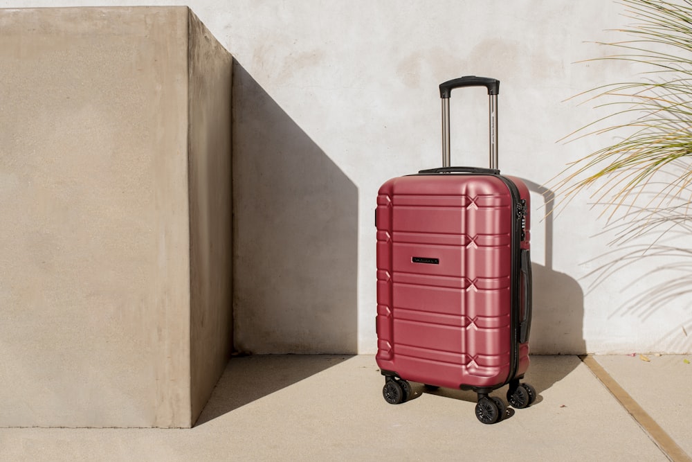 a red piece of luggage sitting next to a plant