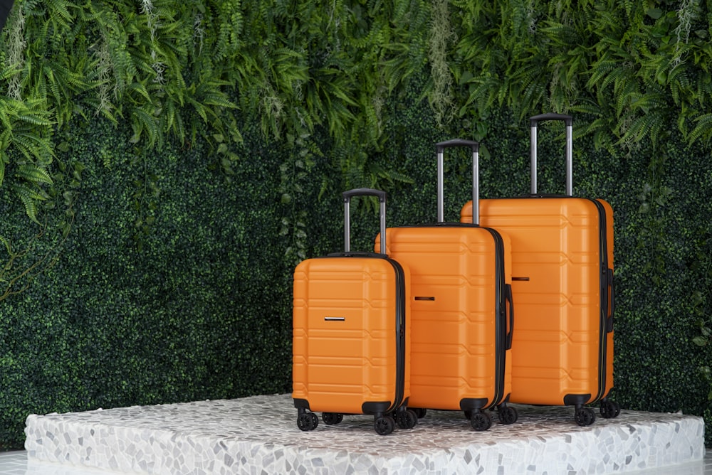 three orange suitcases sitting on a pedestal in front of a green wall