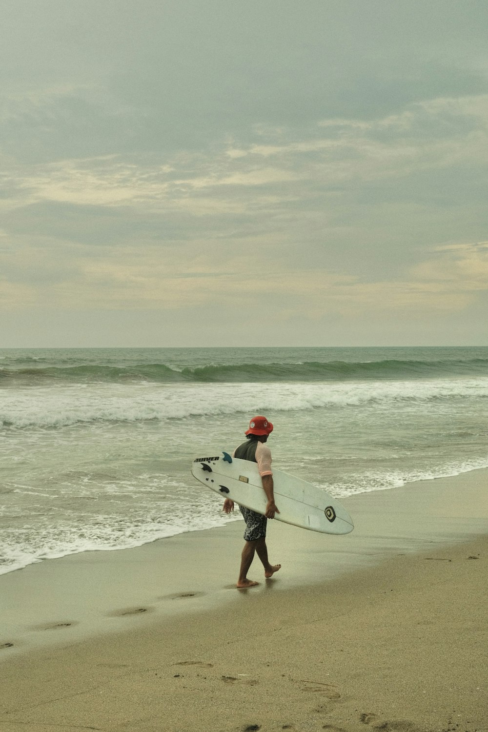 a man walking along the beach with a surfboard