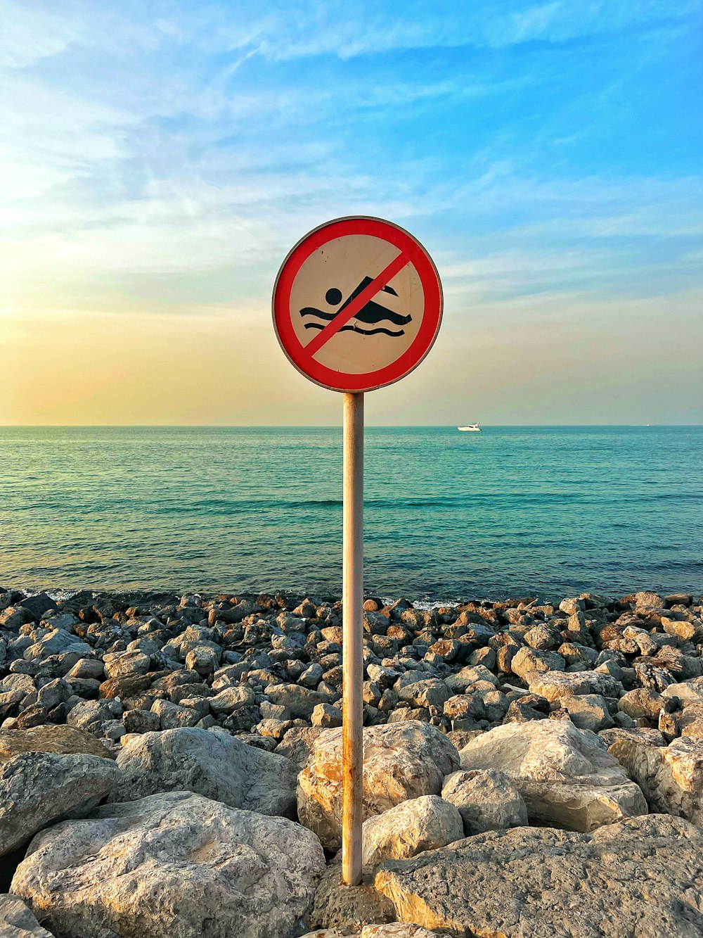 a red and white sign sitting on top of a rocky beach