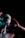 A person with skin covered in textured paint holds their head with both hands. The lighting creates a dramatic effect with shadows and highlights using red and green hues. The person appears introspective and the surrounding darkness enhances the mysterious atmosphere.