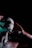 A person with skin covered in textured paint holds their head with both hands. The lighting creates a dramatic effect with shadows and highlights using red and green hues. The person appears introspective and the surrounding darkness enhances the mysterious atmosphere.