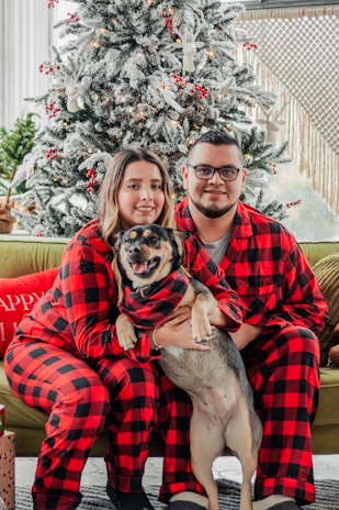 a man and a woman in matching pajamas pose with a dog in front of a