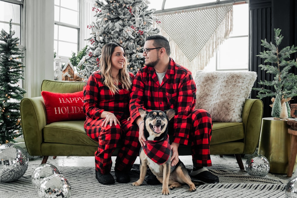 a man and woman in pajamas sitting on a couch with a dog