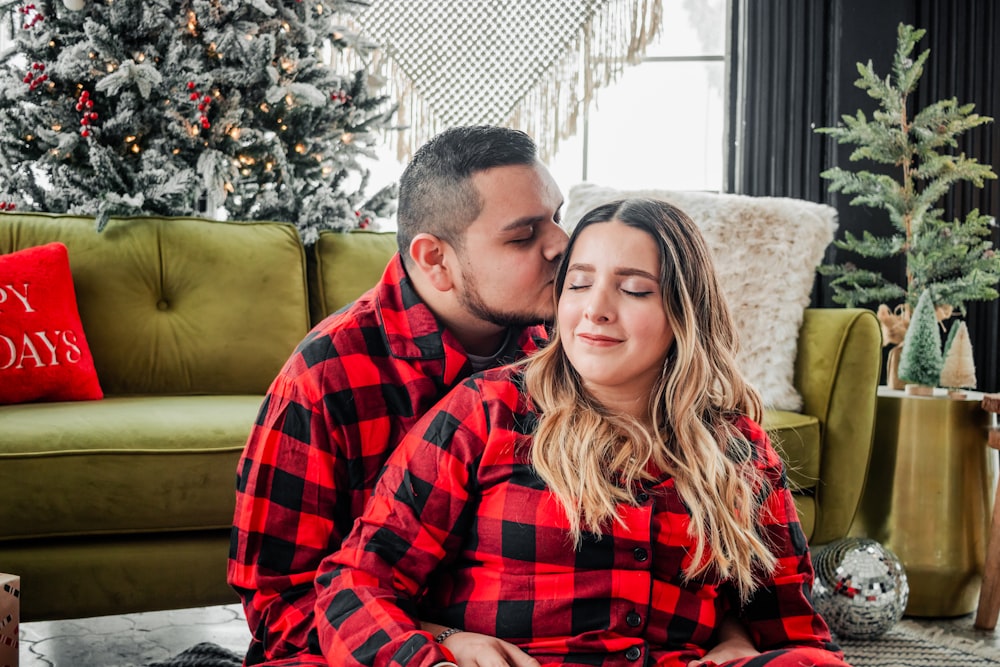 a man and woman sitting on a couch in front of a christmas tree