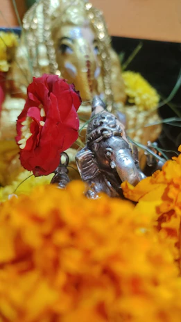 A brass Ganpati statue placed on a wooden shelf surrounded by marigold flowers and traditional decor.