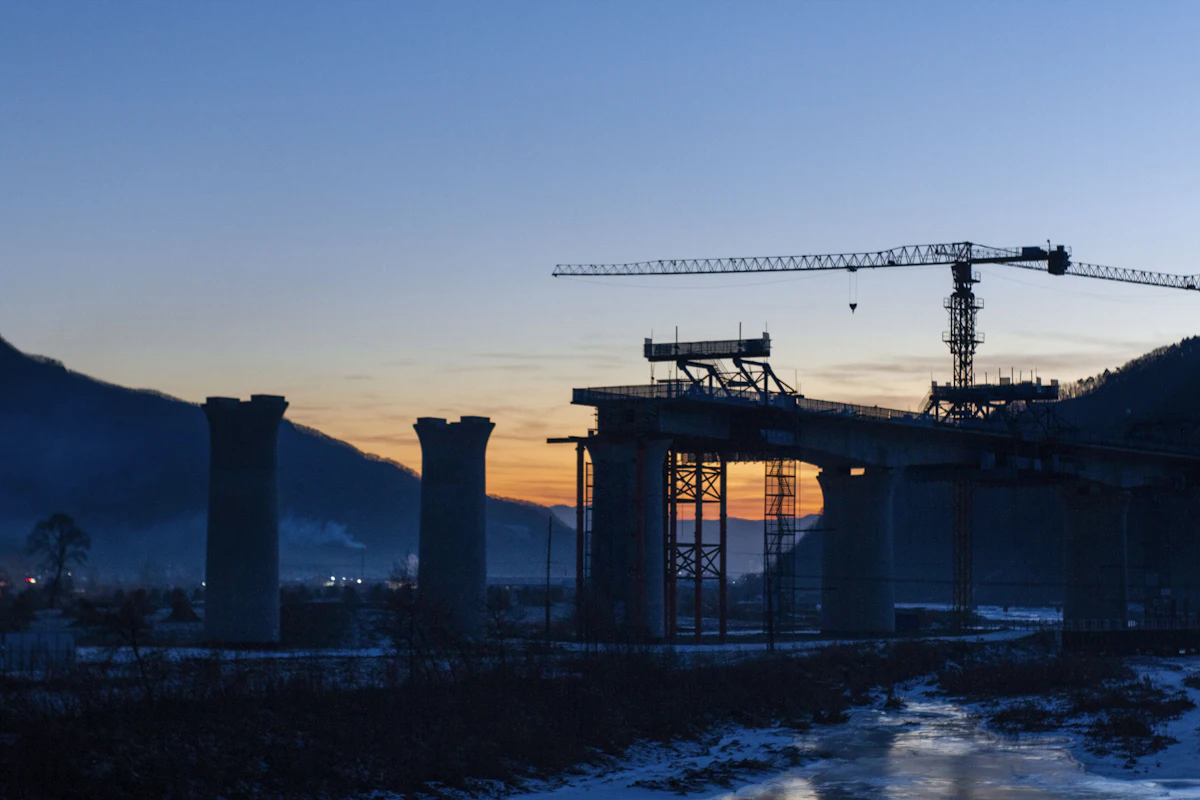 Bridge construction at dusk with a tower crane and exposed piers — the response-mobilization look of an emergency scour repair