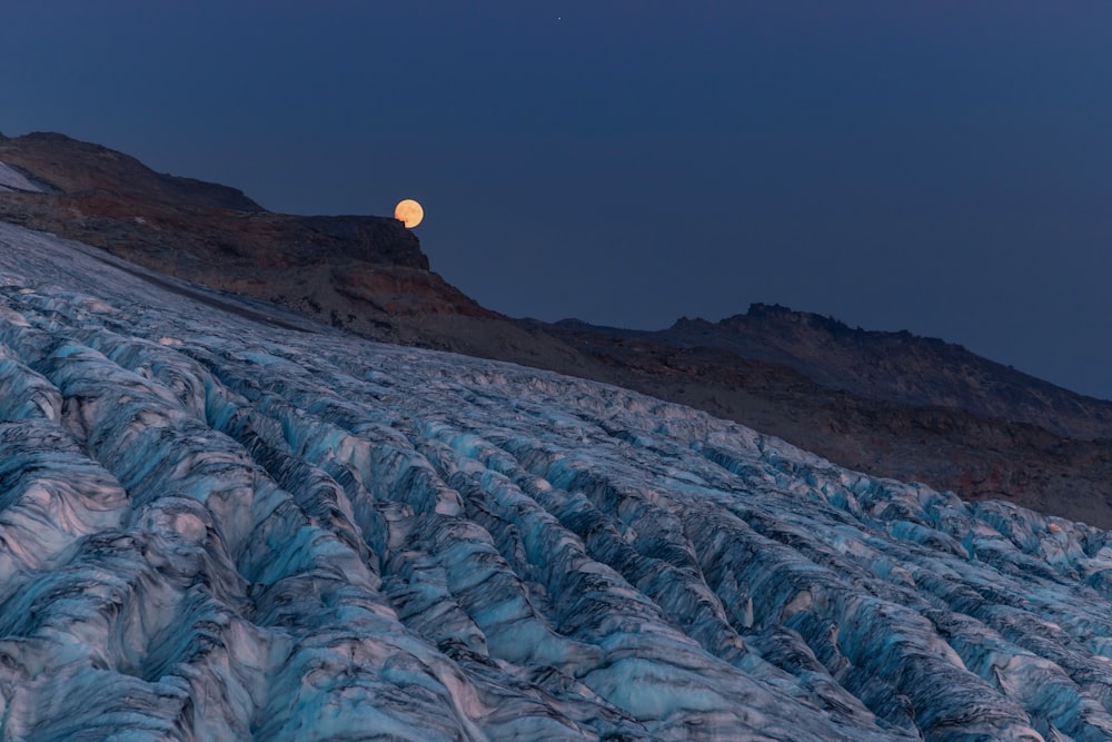 a full moon rising over a glacier with mountains in the background