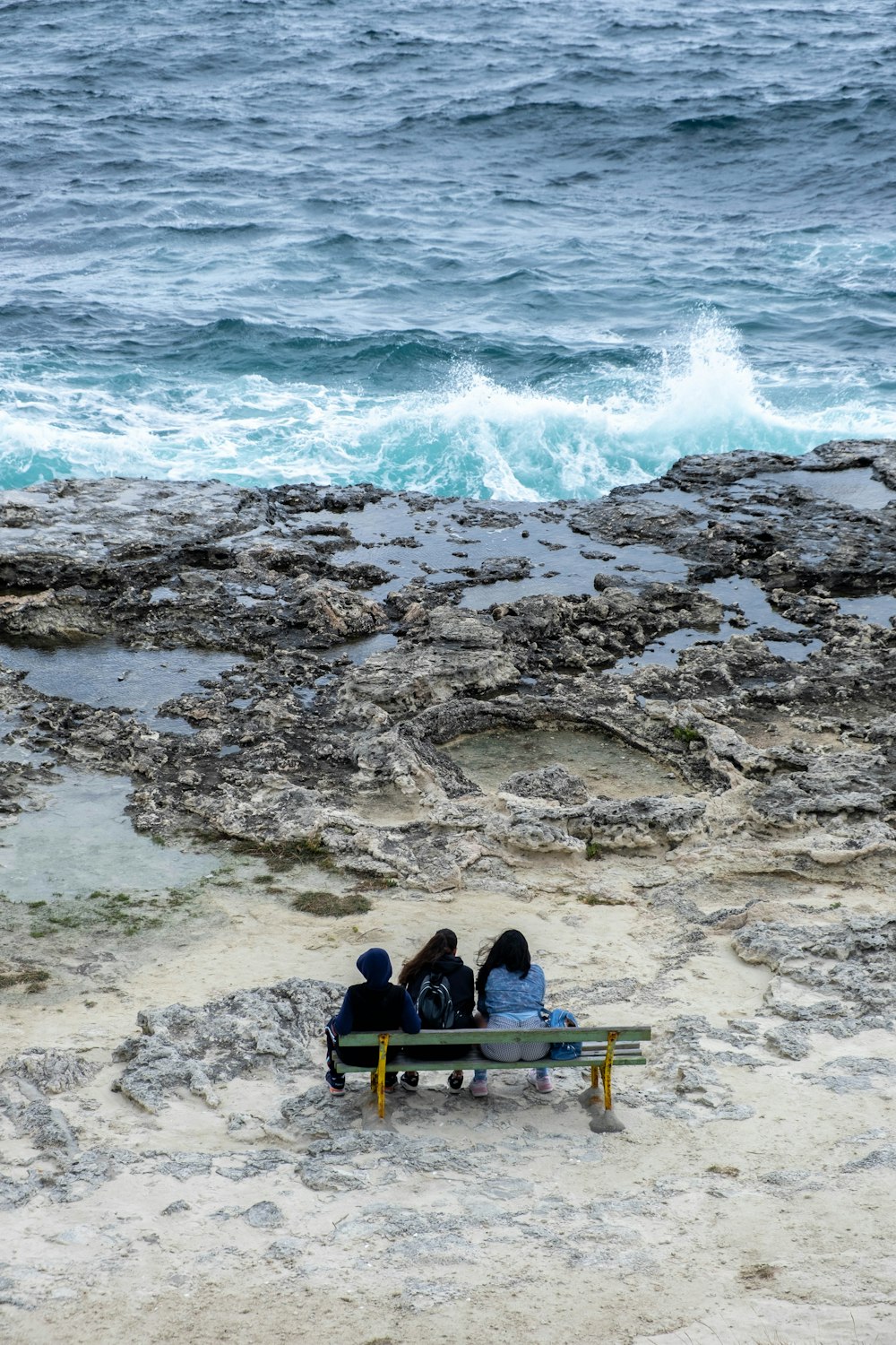 three people sitting on a bench near the ocean