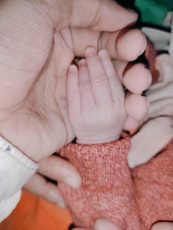 A tiny baby wearing a knitted hat, gently cradled in delicate hands.
