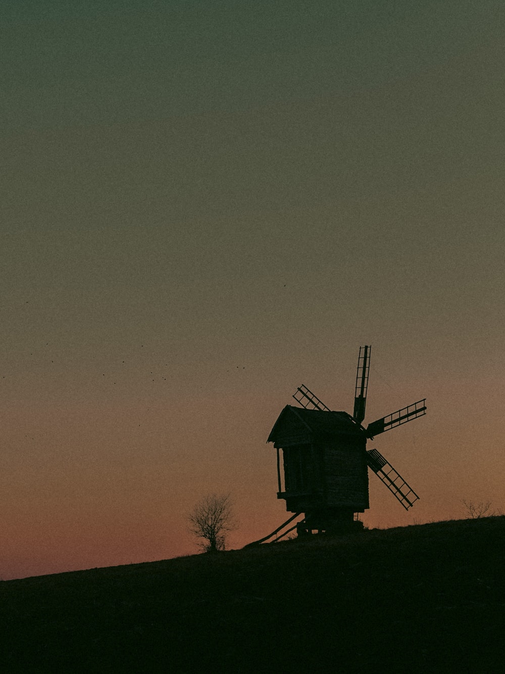 a windmill sitting on top of a hill at sunset