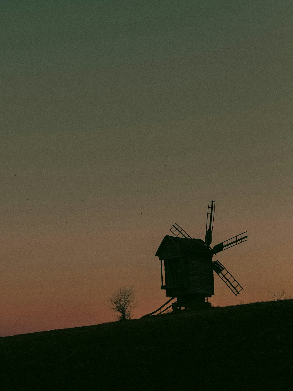 a windmill sitting on top of a hill at sunset