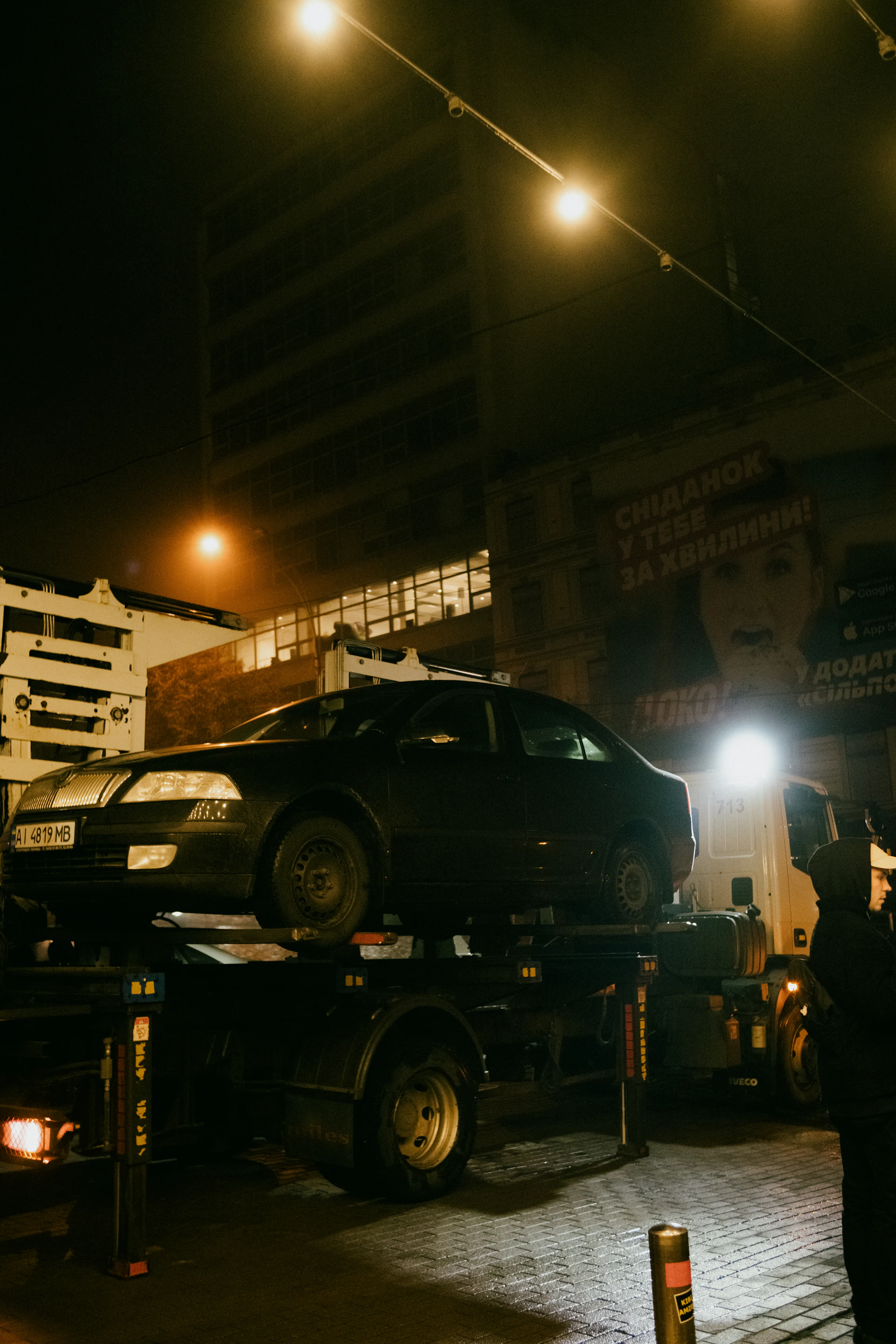 Flatbed tow truck recovering a car on a city road at night
