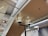 The image captures an indoor setting with a ceiling made of beige-colored panels. Two modern cube-shaped ceiling lights are prominently visible. A net is installed above the ceiling, which may serve as a safety feature. In the background, a snowman decoration with a hat is partially visible, adding a playful element to the environment. Closed metal shutters cover the walls on one side, and a digital sign is attached to the wall.