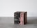 A cube-shaped product box with elegant black and pink design elements, featuring text and logos related to tea. The box is placed on a simple gray surface with a minimalist background.