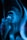 A person appears to be immersed in swirling patterns of blue light, with hands near the face. The image has an ethereal and surreal quality created by the long exposure or digital effect.