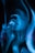 A person appears to be immersed in swirling patterns of blue light, with hands near the face. The image has an ethereal and surreal quality created by the long exposure or digital effect.