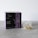 A box labeled 'Crystal Tea Elixir Detox Agata' is prominently displayed, featuring a sleek design with large overlapping text and a small logo of a leaf. Beside the box, there is a transparent pyramid-shaped tea bag containing a variety of loose leaf herbs.