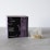 A box labeled 'Crystal Tea Elixir Detox Agata' is prominently displayed, featuring a sleek design with large overlapping text and a small logo of a leaf. Beside the box, there is a transparent pyramid-shaped tea bag containing a variety of loose leaf herbs.