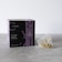 A box labeled 'Crystal Tea Elixir Detox Agata' is prominently displayed, featuring a sleek design with large overlapping text and a small logo of a leaf. Beside the box, there is a transparent pyramid-shaped tea bag containing a variety of loose leaf herbs.