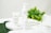 Three skincare product bottles are displayed on a white circular tray. The background includes fresh green leaves, emphasizing a natural theme. The surface is a marble-like white, adding elegance.