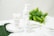 Three skincare product bottles are displayed on a white circular tray. The background includes fresh green leaves, emphasizing a natural theme. The surface is a marble-like white, adding elegance.