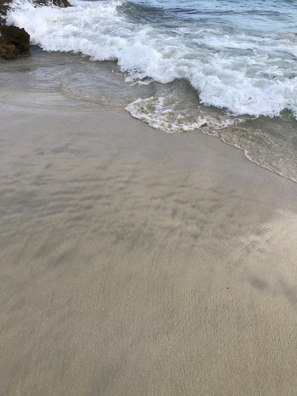 a sandy beach next to the ocean with waves coming in