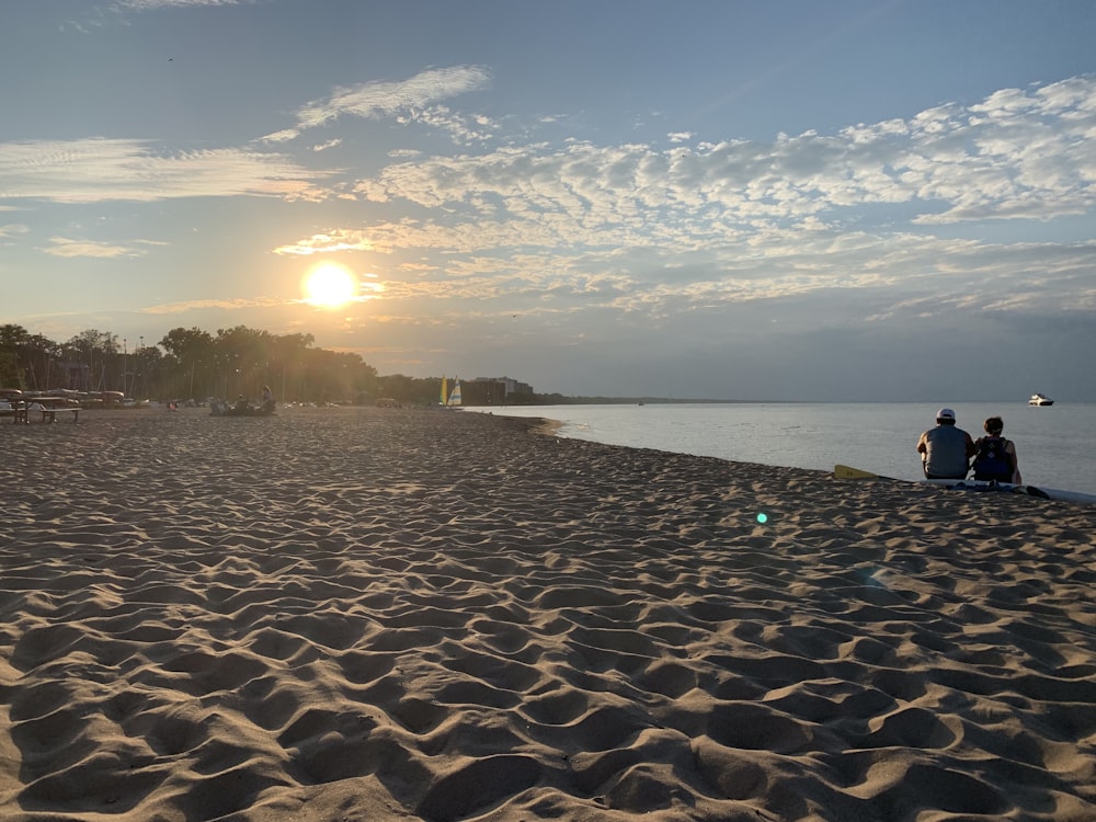 a couple of people sitting on top of a sandy beach