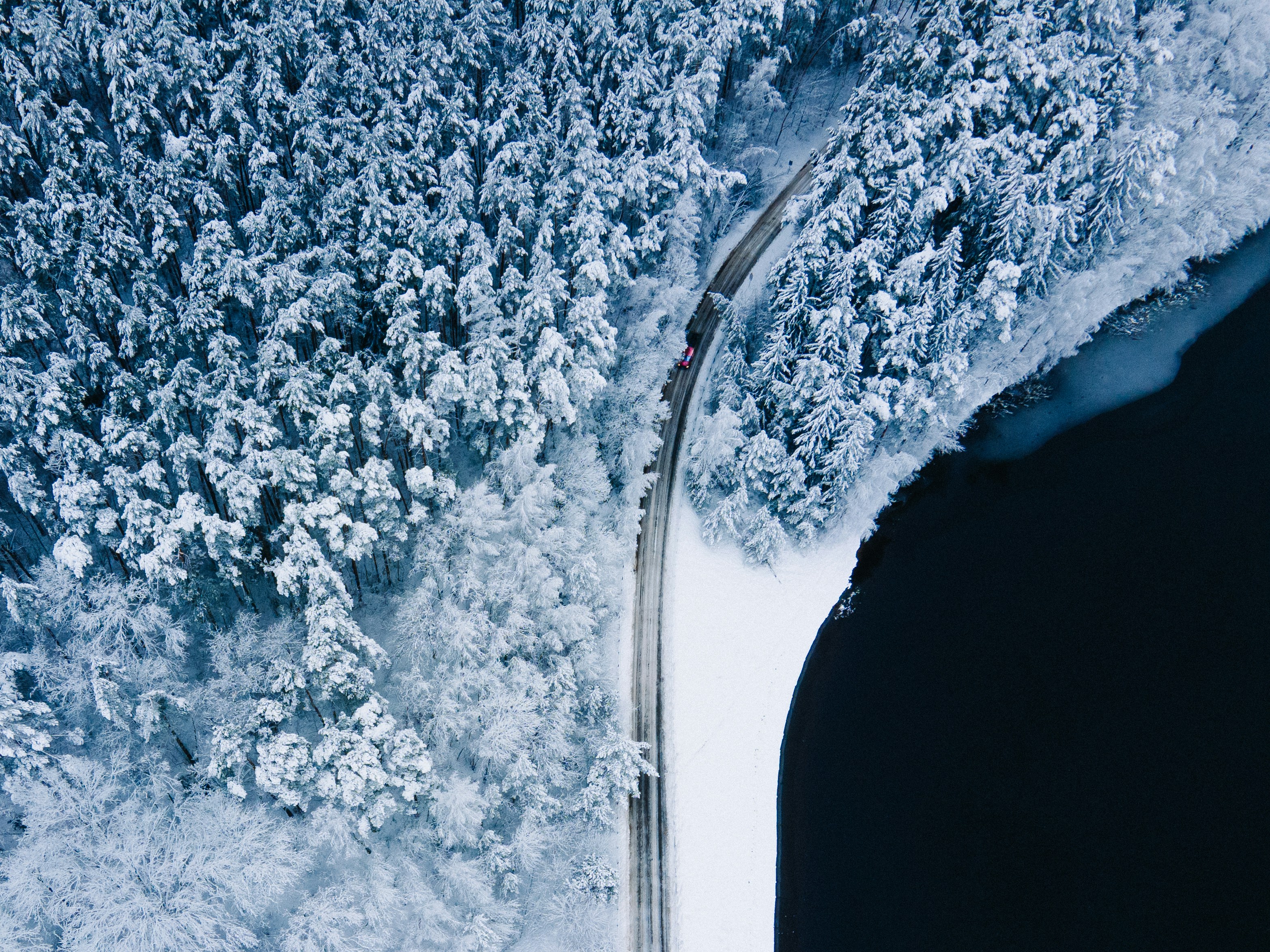 an aerial view of a road surrounded by snow covered trees
