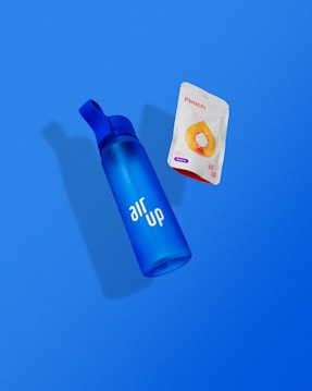 A blue bottle with the words 'air up' printed on it is positioned next to a packet labeled 'Peach' which features an image of a peach slice. Both items are set against a solid blue background.