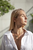 A smiling woman wearing layered necklaces and bracelets in natural sunlight.