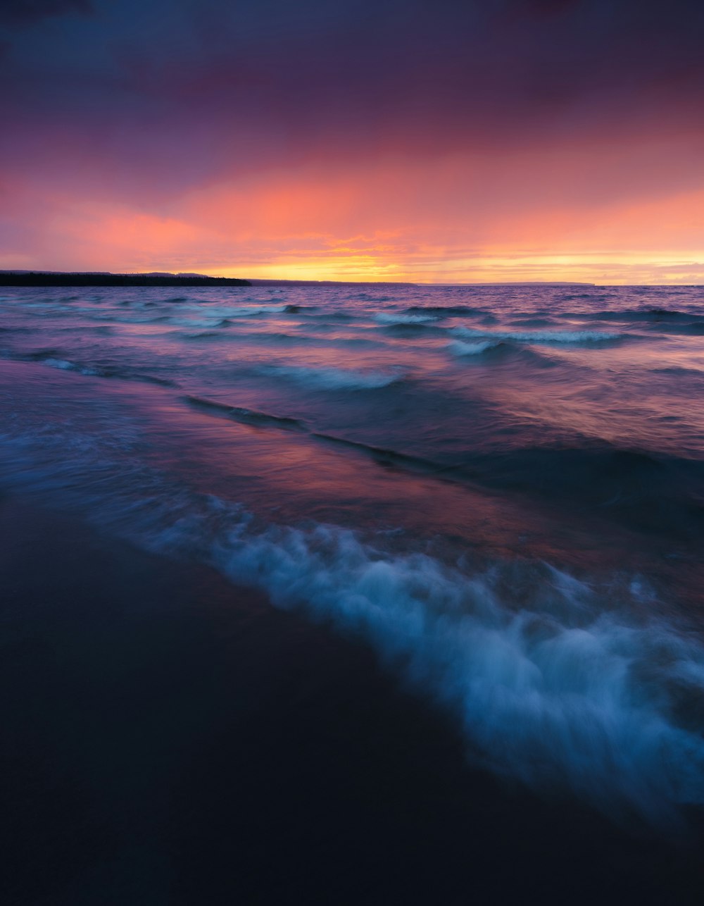 a sunset over the ocean with waves coming in