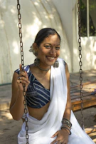 A candid shot of a girl sitting on a traditional swing, dressed in a beige and gold lehenga, with marigold garlands in the background.