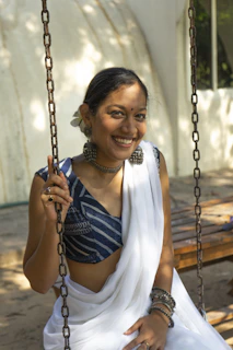 A candid shot of a girl sitting on a traditional swing, dressed in a beige and gold lehenga, with marigold garlands in the background.