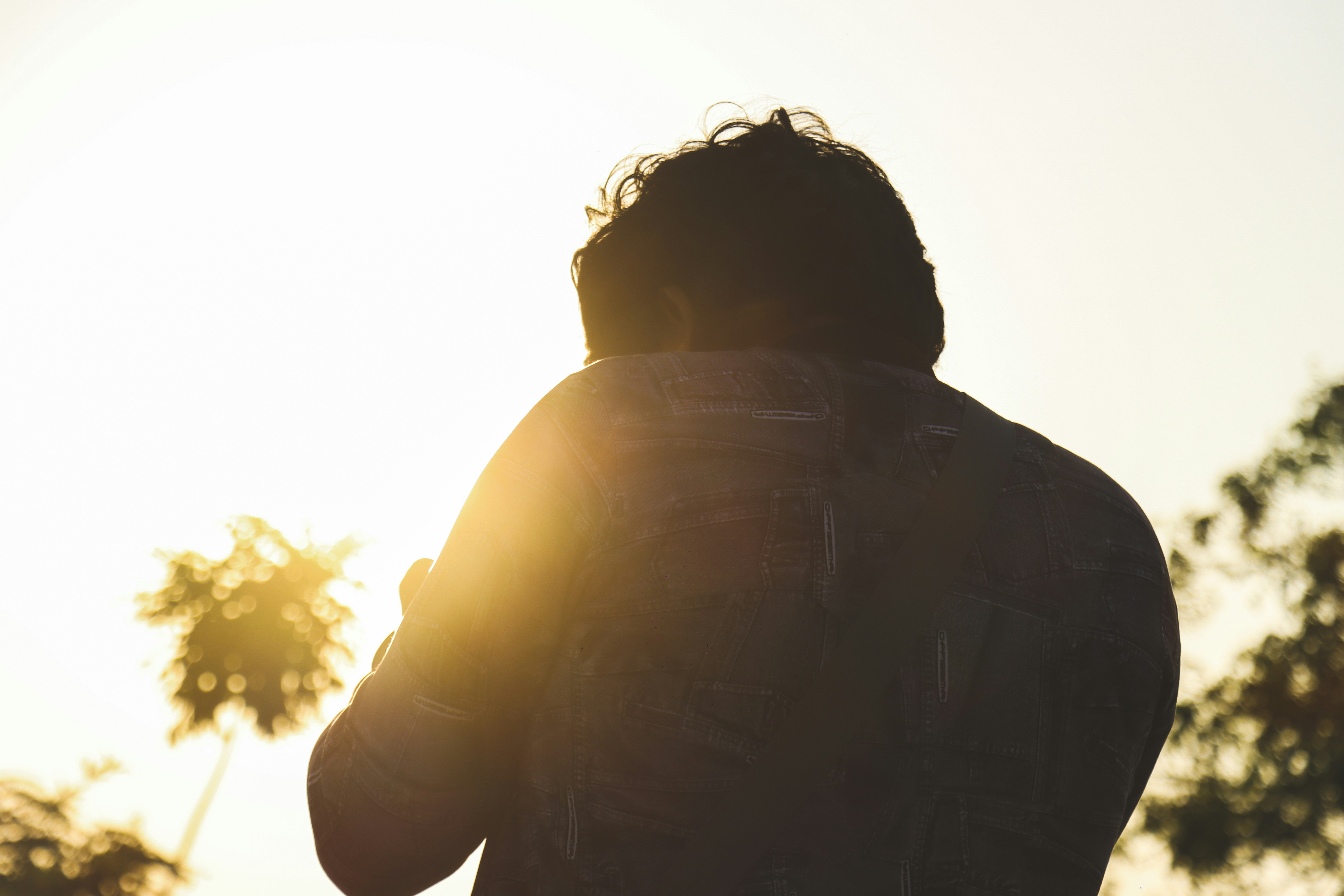a man standing in front of the sun with his back to the camera