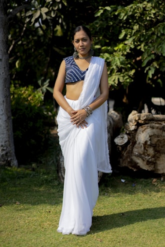 A woman wearing a Kunbi saree without blouse, standing in a lush green field