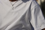 A close-up of a person wearing a plain white t-shirt featuring minimal black text with diagrams indicating 'better' and 'worse'. The person is also wearing a silver chain necklace with a cross pendant.