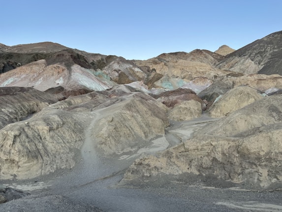 A landscape of multicolored hills and mounds, featuring pastel hues of pink, green, and blue against a backdrop of rocky slopes and a clear sky.