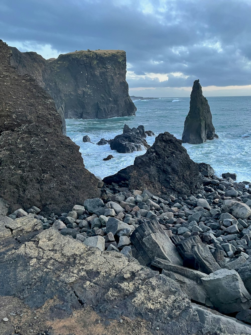 a rocky beach next to the ocean under a cloudy sky