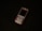 A classic mobile phone with a numeric keypad and small screen rests on a dark surface. The phone has a metallic finish with a black display and visible branding near the earpiece.