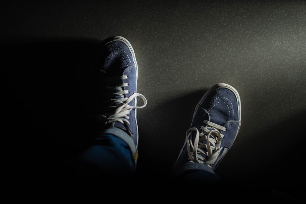 a person's feet in blue sneakers on a black surface