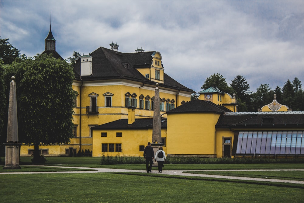 two people walking in front of a yellow building