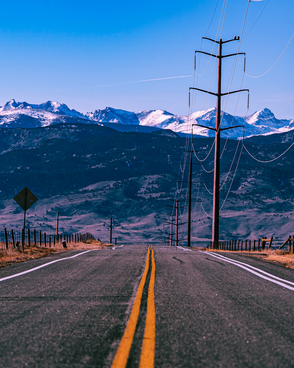 Two-lane road winding through mountainous landscape with yellow lines and parallel power lines stretching into