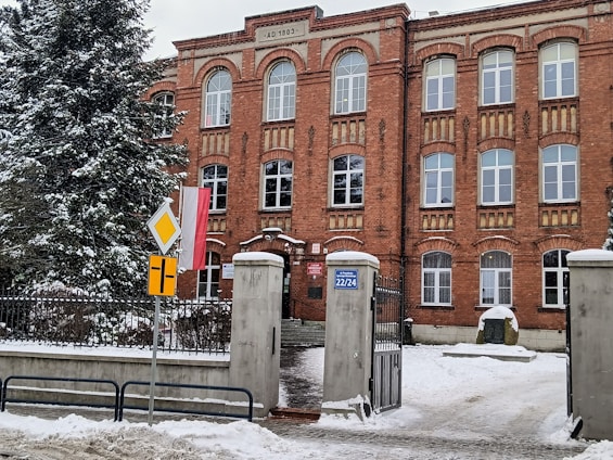 Akademik szkolny z drewnianą konstrukcją i dwuspadowym dachem na tle zieleni.