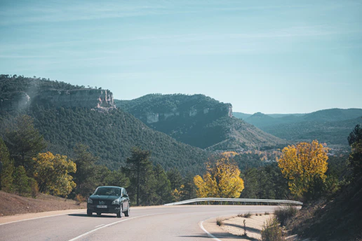 A comfortable car driving on a scenic highway surrounded by green hills and blue skies.