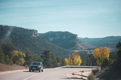 A taxi cruising along a winding road surrounded by lush green hills.