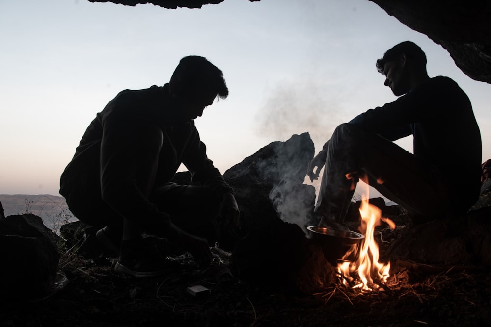 a couple of men sitting next to a fire